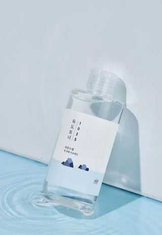 Flacon ROUND LAB 1025 Dokdo Toner pose sur surface bleue mouillee avec ondulations d'eau
