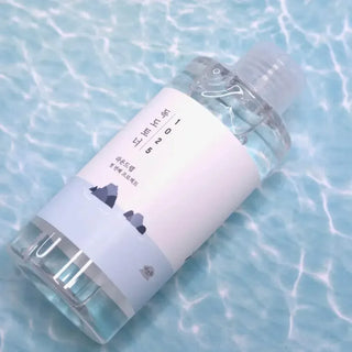 Flacon ROUND LAB 1025 Dokdo Toner allonge sur une surface d'eau turquoise