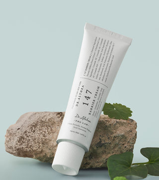 Tube Dr.Althea 147 Barrier Cream 50ml appuyé contre une pierre avec feuilles vertes sur fond gris-bleu