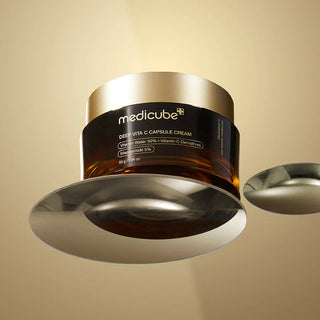 Pot Medicube Deep Vita C Capsule Cream en suspension au-dessus de disques metalliques dores