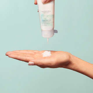 Wella Nutricurls Cleansing Conditioner - main recevant la creme versee du tube sur fond menthe