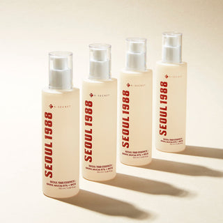 Quatre flacons pompe KSECRET Seoul 1988 Essence Snail Mucin alignes avec ombres sur fond creme