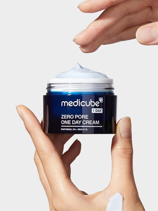 Mains tenant le pot ouvert Medicube Zero Pore One Day Cream montrant la creme bleu clair a l'interieur