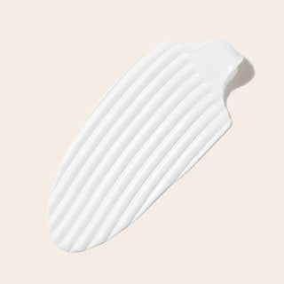 Trace epaisse de creme blanche striee sur fond beige, texture creme coiffante Boucleme anti-frisottis