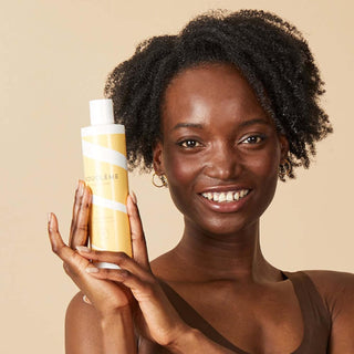 Modele aux cheveux boucles tenant le flacon Boucleme Curl Conditioner orange sur fond beige