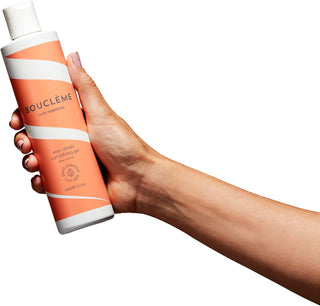 Main tenant le flacon orange Boucleme Curl Defining Gel 300 ml sur fond blanc