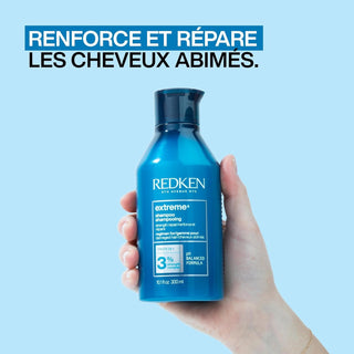 Main tenant le flacon bleu REDKEN Extreme Shampoo 300ml sur fond bleu, mention renforce et repare
