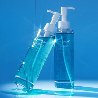 Deux flacons Medicube Zero Pore Cleansing Oil poses sur fond bleu avec reflets lumineux et eclats