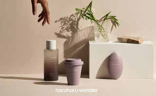 Haruharu Wonder Black Rice Toner, gobelet et baume ovale poses sur un decor beige avec vase et verdure