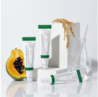 Trois formats du serum AXIS-Y Dark Spot Correcting Glow Serum avec papaye coupee, riz et erlenmeyer en verre