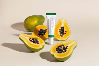Tube AXIS-Y Dark Spot Correcting Glow Serum entoure de papayes fraiches coupees sur fond beige clair