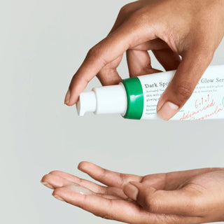 Mains pressant le tube AXIS-Y Dark Spot Correcting Glow Serum, goutte de serum tombant dans la paume