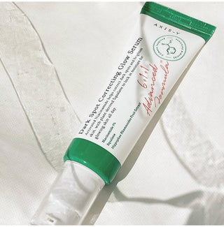 AXIS-Y Dark Spot Correcting Glow Serum 50ml pose a plat sur tissu blanc avec trainee de serum transparent