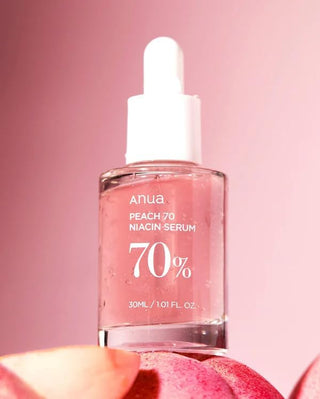 ANUA Peach 70 Niacin Serum - gros plan du flacon rose pose sur des tranches de peche fraiche