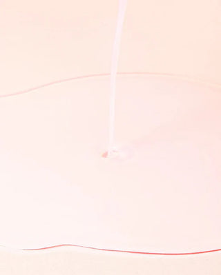 Texture laiteuse translucide du toner ANUA Peach 77 versee en filet sur fond rose pale