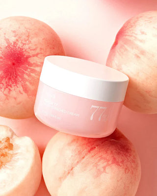 Pot ANUA Peach 77 Niacin Enriched Cream pose parmi des peches fraiches sur fond rose