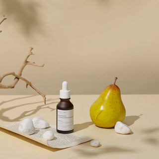MARY&MAY Niacinamide Chaenomeles Serum - flacon pose pres d'une poire et galets blancs sur fond beige