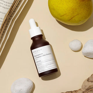 MARY&MAY Niacinamide Chaenomeles Serum - flacon debout entre galets, livre et poire sur fond beige