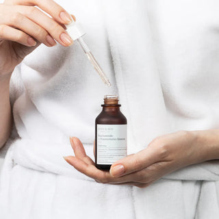 MARY&MAY Niacinamide Chaenomeles Serum - main tenant la pipette au-dessus du flacon ouvert, peignoir blanc