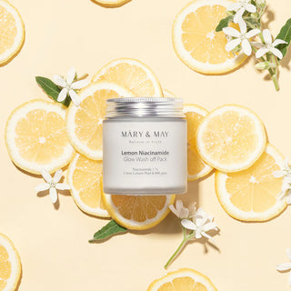 Pot MARY&MAY Lemon Niacinamide Glow Wash Off Pack pose sur des tranches de citron avec fleurs blanches