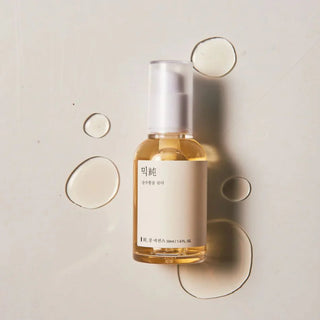 Flacon Mixsoon Bean Essence vue du dessus avec gouttes de texture doree sur fond beige clair