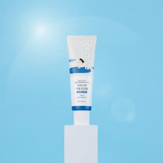 Tube Round Lab Birch Juice Sun Cream pose sur socle blanc avec lumiere et fond bleu ciel