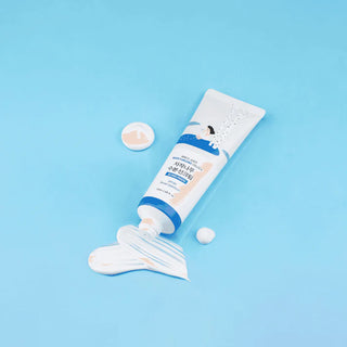 Tube ouvert Round Lab Birch Juice Sun Cream avec texture blanche coulante sur fond bleu