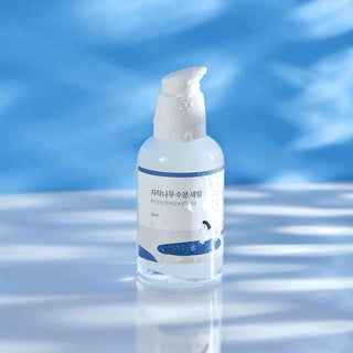 Round Lab Birch Juice Serum avec mousse sur la pompe et reflets aquatiques en arriere-plan bleu