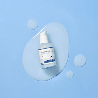 Flacon pompe Round Lab Birch Juice Serum entoure de gouttes de texture transparente sur fond bleu
