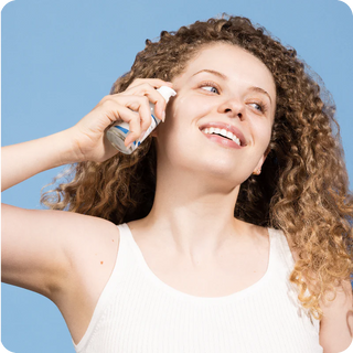 Femme souriante aux cheveux boucles appliquant le serum Round Lab Birch Juice sur son visage