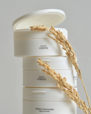 Pile de pots Beauty of Joseon Radiance Cleansing Balm ouverts avec des epis de riz sur fond gris