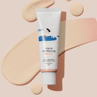 Round Lab Birch Tone-Up Sunscreen SPF50+ sur fond peche avec larges traces de texture rosee