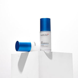 Flacon et capuchon bleu Medicube Zero Pore Serum 2.0 separes sur un socle blanc minimaliste