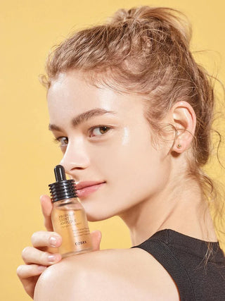 Modele tenant le flacon COSRX Propolis Light Ampoule pres du visage sur fond jaune