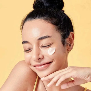 Jeune femme souriante avec touche de COSRX Propolis Light Cream sur la joue, fond jaune