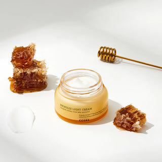 COSRX Propolis Light Cream pot ouvert entoure de rayons de miel et cuillere a miel doree