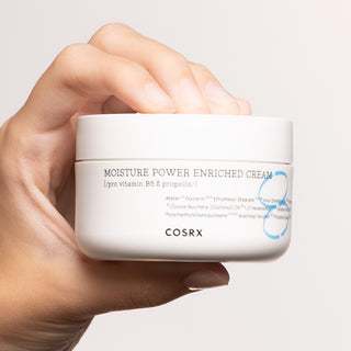 COSRX Hydrium Moisture Power Enriched Cream pot blanc tenu dans une main sur fond clair