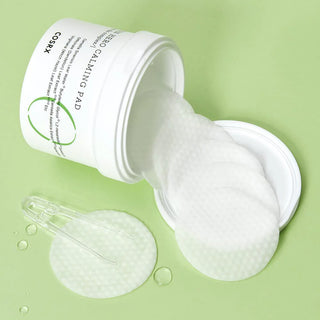 Pot COSRX Green Hero Calming Pad renverse sur fond vert avec pads et pince transparente