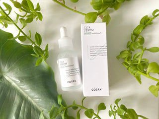 Flacon et boite COSRX Pure Fit Cica Serum poses parmi des feuilles vertes tropicales et plantes