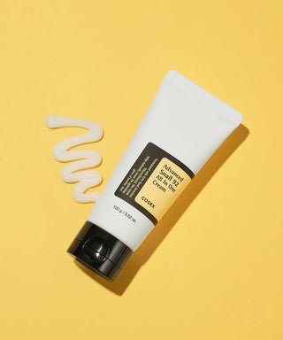 COSRX Advanced Snail 92 Cream incline sur fond jaune avec texture creme onctueuse etalee