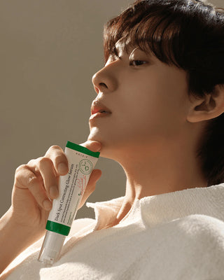 Modele masculin tenant le tube AXIS-Y Dark Spot Correcting Glow Serum pres du visage, eclairage dore