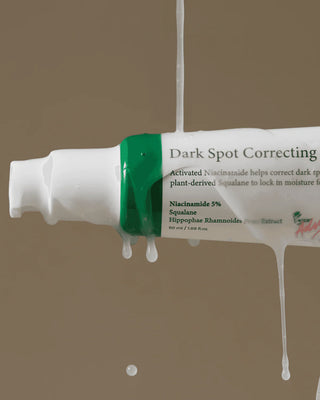 Tube AXIS-Y Dark Spot Correcting Glow Serum suspendu avec serum liquide coulant sur fond brun dore