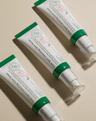 Trois tubes AXIS-Y Dark Spot Correcting Glow Serum alignes en diagonale sur fond beige clair