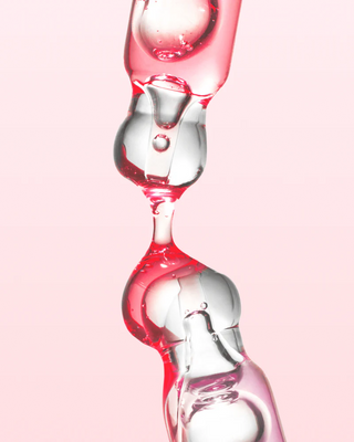 Bulles de gel rose et transparent du serum ANUA Niacinamide 10+ TXA 4 en suspension sur fond rose