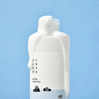 Round Lab 1025 Dokdo Lotion - haut du flacon blanc avec lotion debordante coulant sur l'etiquette, fond bleu