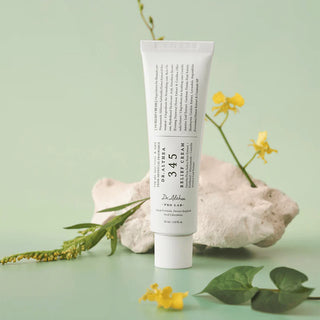 Tube DR.ALTHEA 345 Relief Cream pose contre une pierre blanche avec fleurs jaunes
