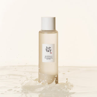 Flacon Beauty of Joseon Glow Replenishing Rice Milk posé au milieu d'une éclaboussure de liquide laiteux