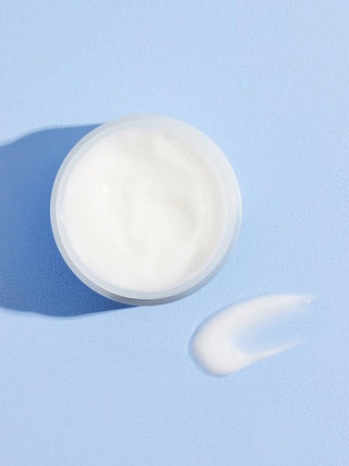 Texture crème blanche fondante de la COSRX Hyaluronic Acid Intensive Cream vue de dessus avec swatch sur fond bleu