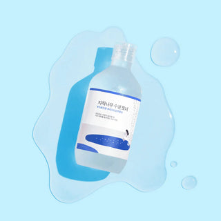 Round Lab Birch Juice Toner flottant dans une flaque d'eau sur fond bleu clair avec bulles
