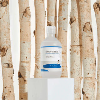 Round Lab Birch Juice Toner pose sur socle blanc devant des troncs de bouleau naturels